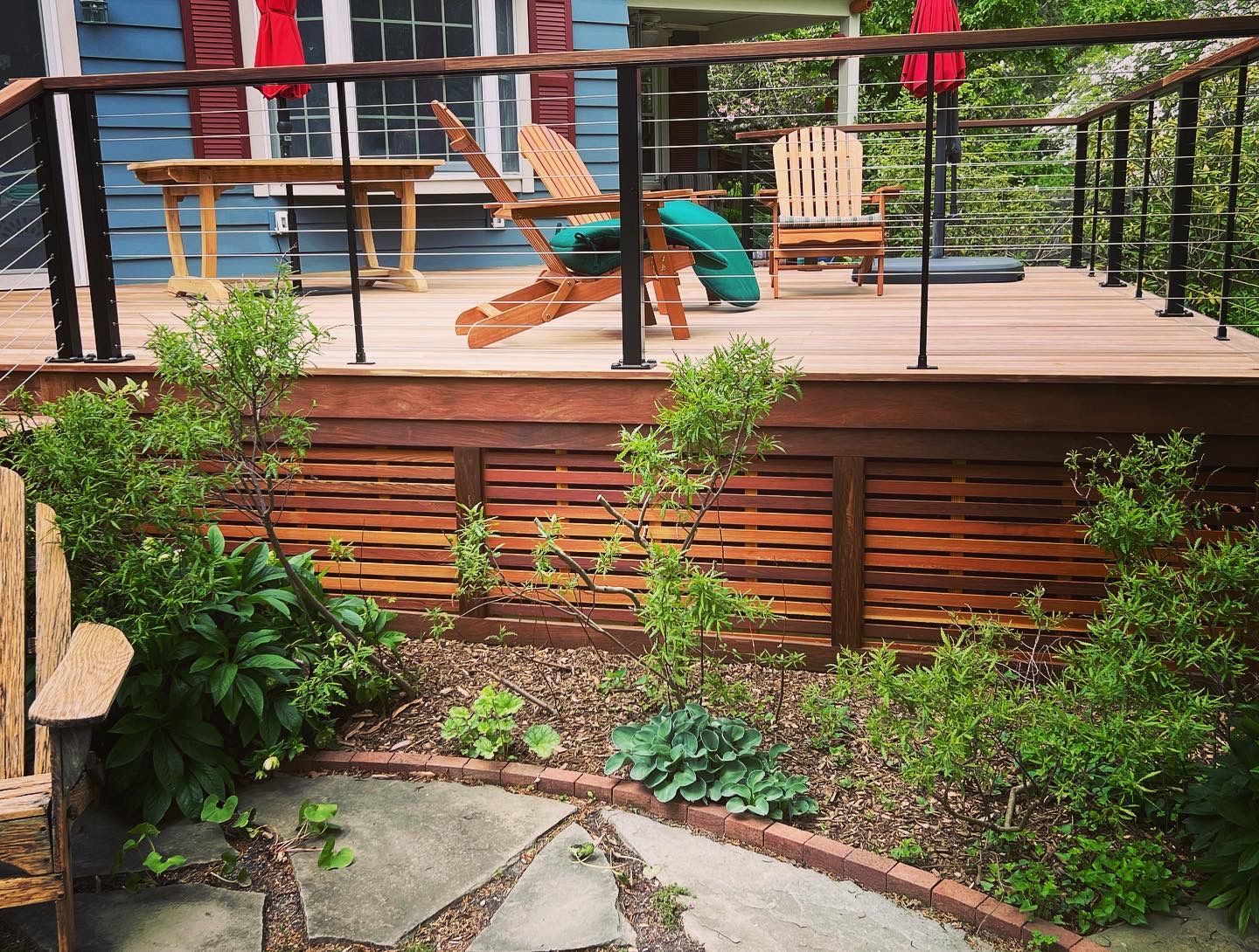Wooden deck with Adirondack chairs, small table, and garden with stone path.