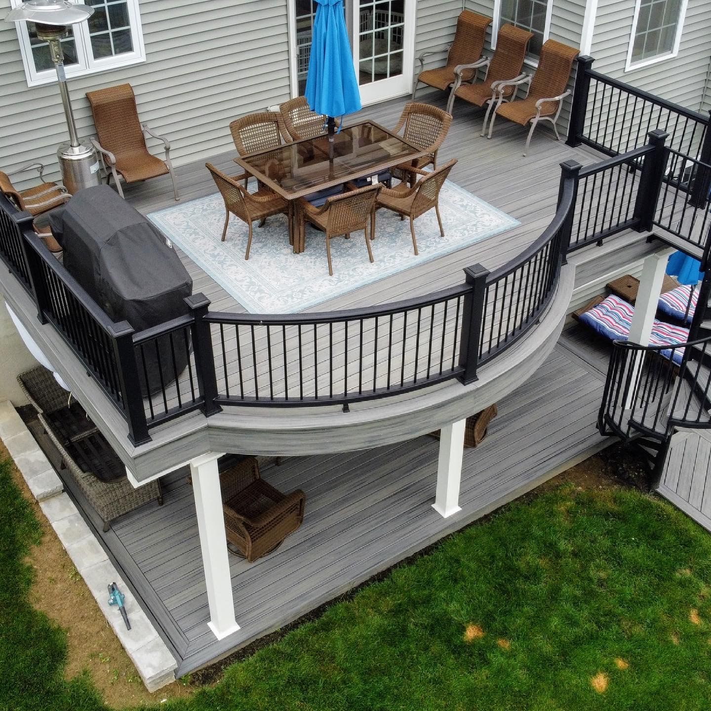 Multi-level gray deck with dining table, chairs, grill, and spiral staircase.