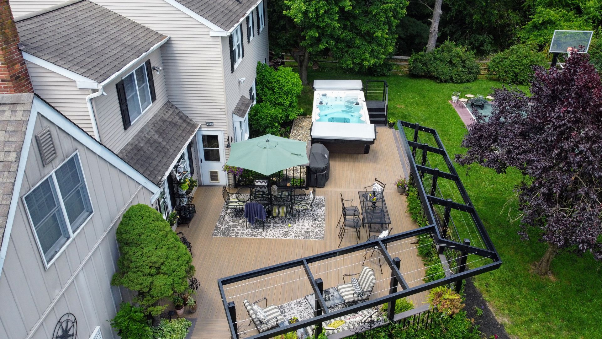 Aerial view of a home's backyard patio with a hot tub, seating area, and lush green lawn.