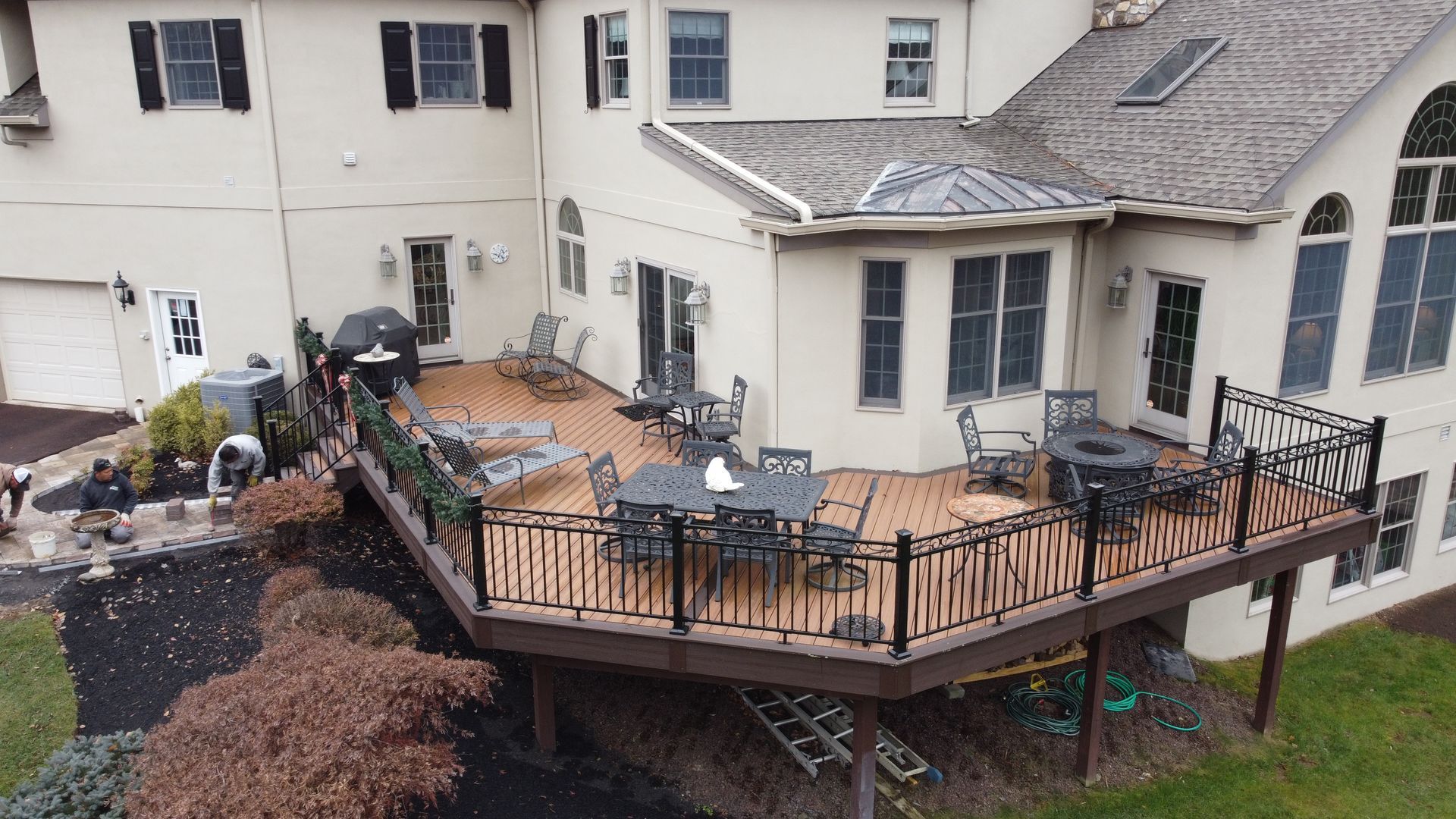 Large house with wooden deck and black railings. Outdoor furniture on the deck, and landscaping in the foreground.
