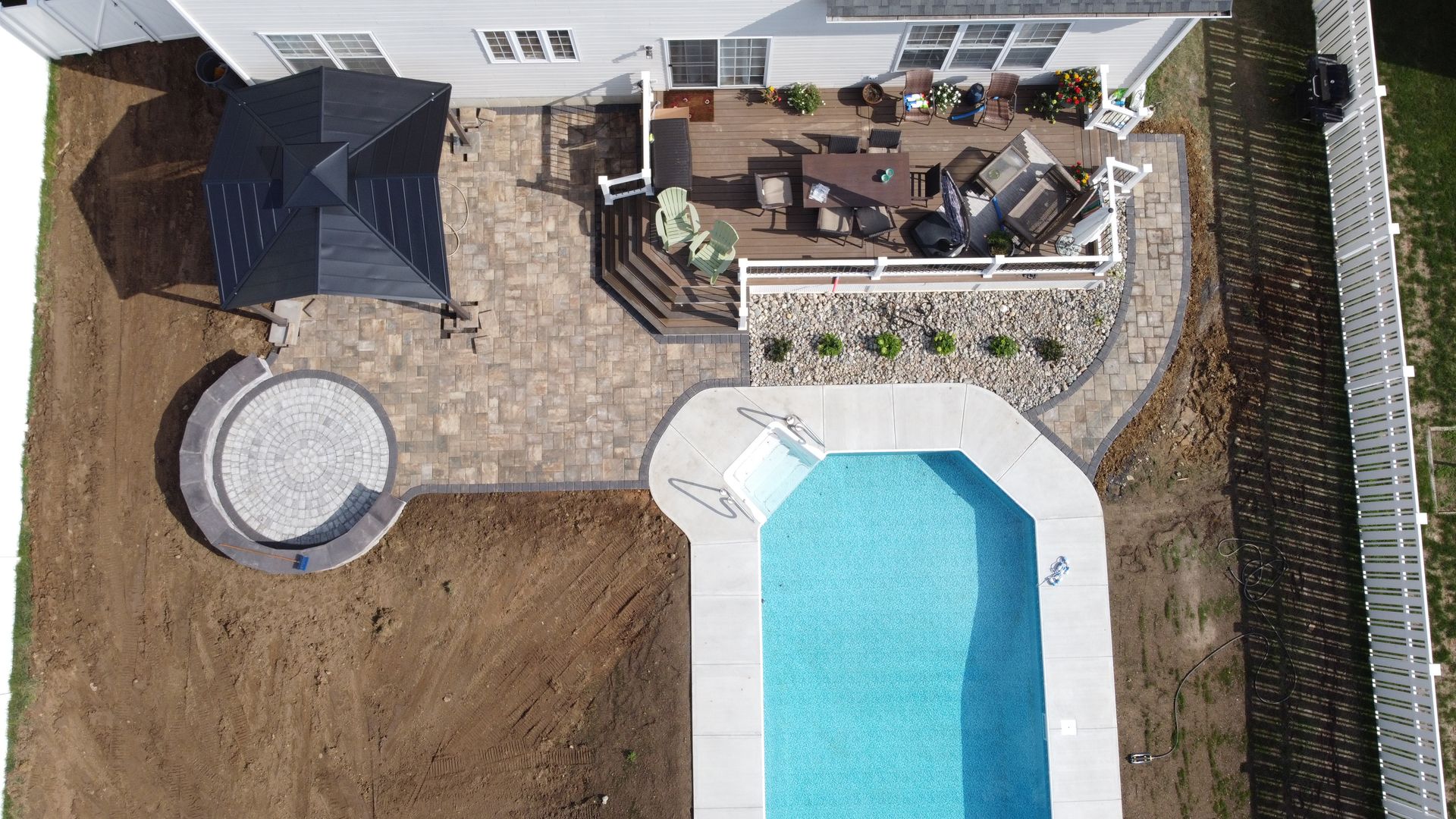 Overhead view of a backyard with a pool, patio, gazebo, and multi-level deck connected by stone pathways.