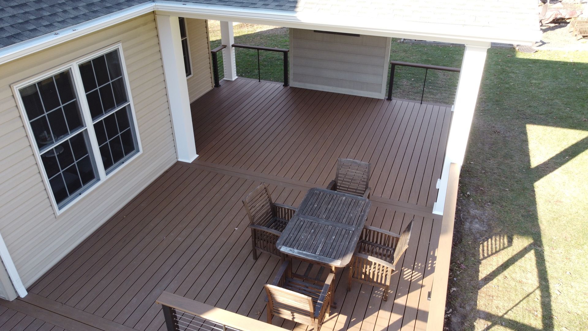 A wooden deck with a table and chairs, attached to a light beige house with a covered area.