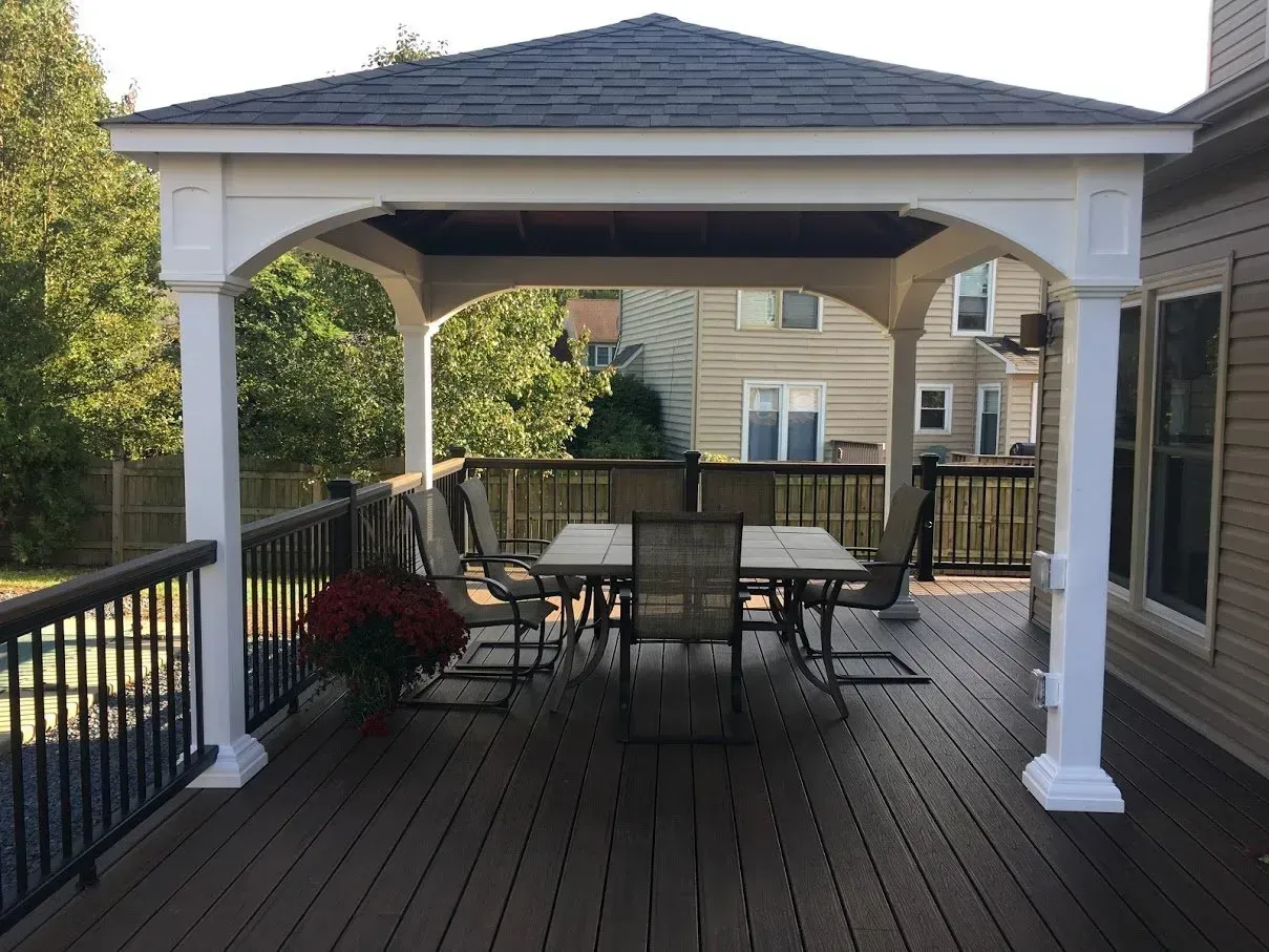 White gazebo with table and chairs on a wooden deck; backyard setting.