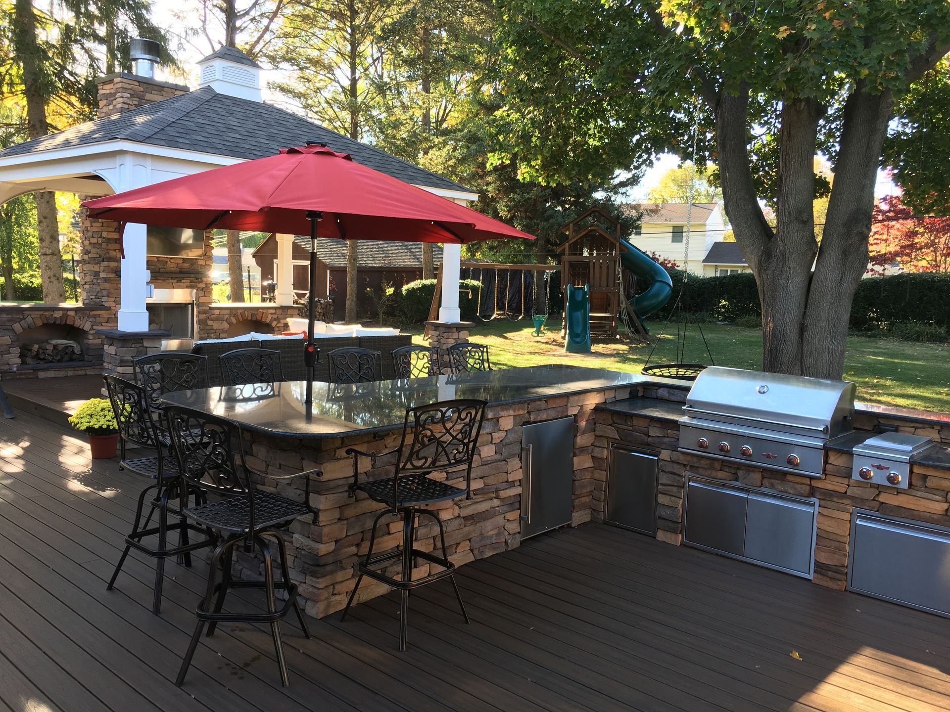 Outdoor kitchen with granite countertop, grill, seating, and red umbrella on a wooden deck.