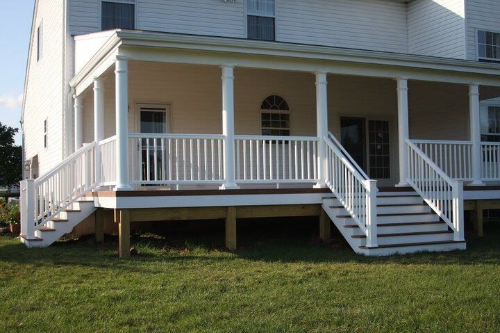 White porch with stairs and railings, attached to a two-story beige house.