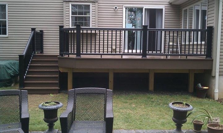 Wooden deck with black railing and stairs leading down to a grassy backyard.