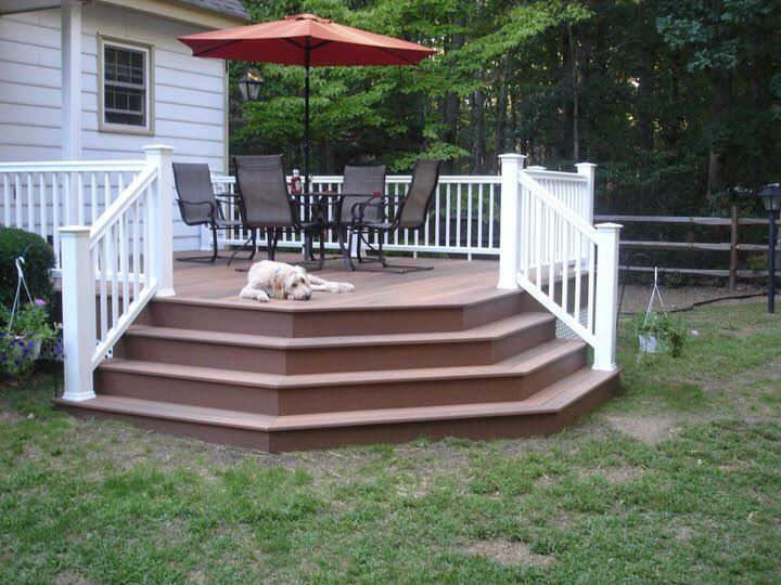 Brown deck with white railing, chairs, umbrella, and dog in backyard.