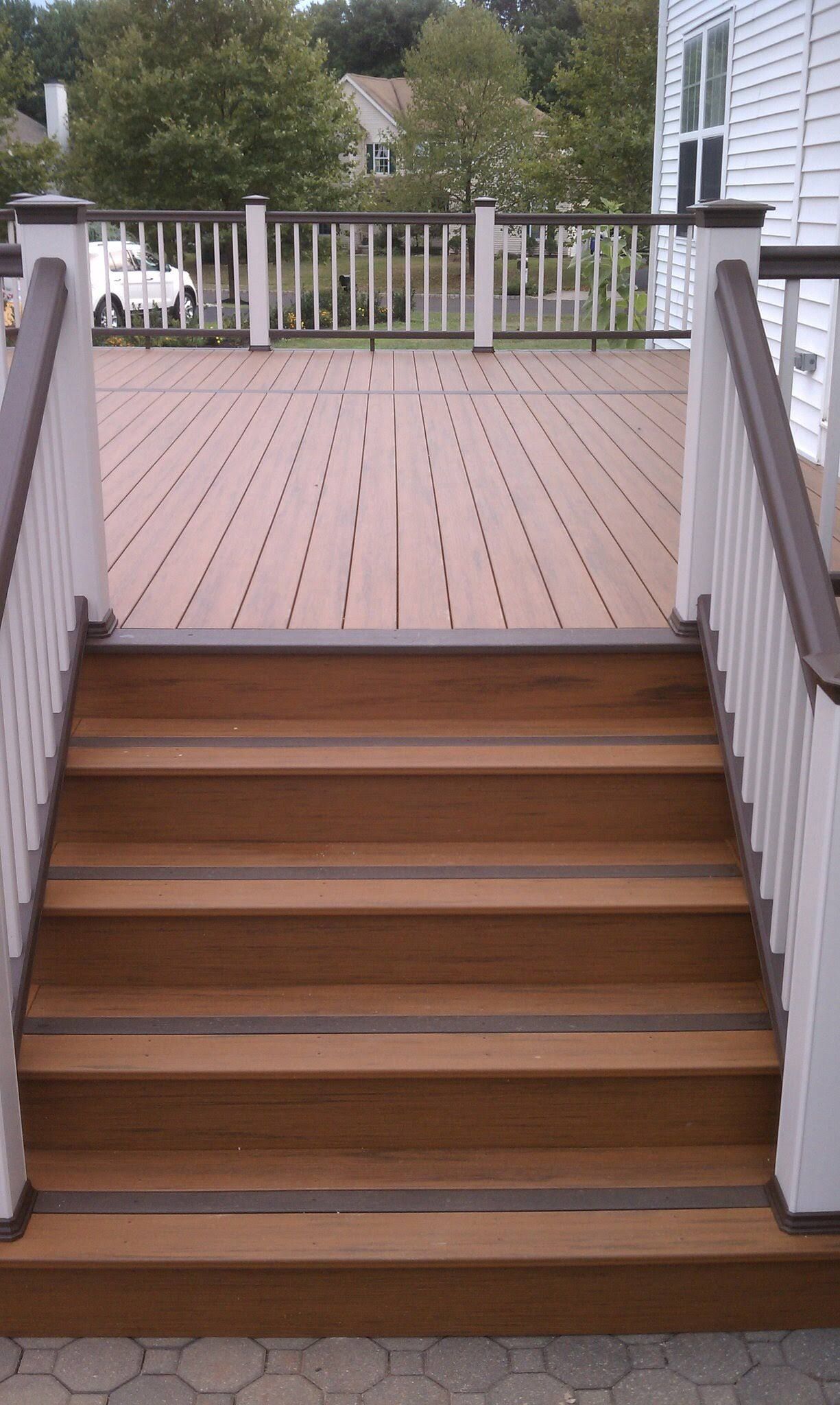 Wooden deck with stairs leading up, white railings, brown wood and deck boards.