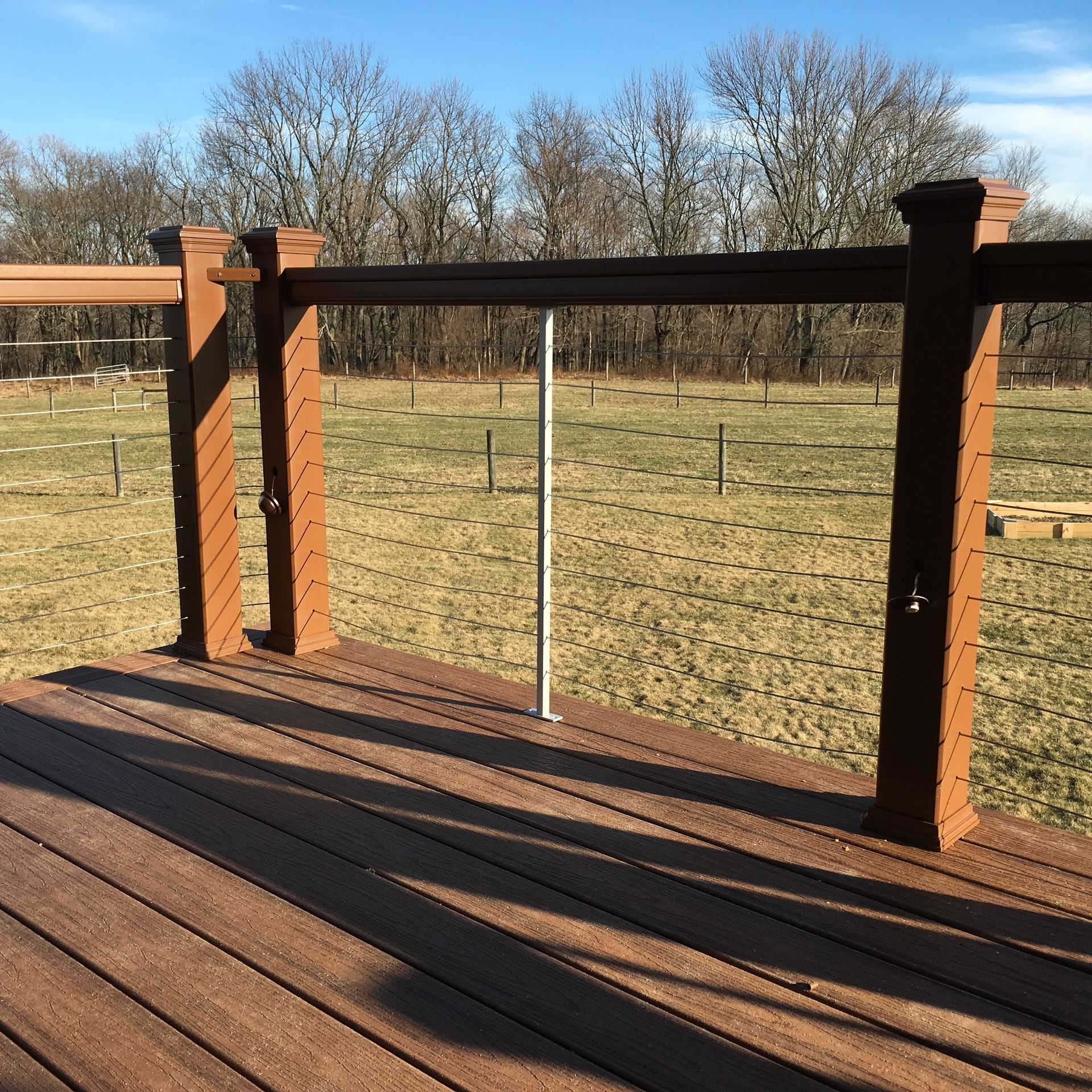 Wooden deck with brown posts and railings, overlooking a grassy field with trees.