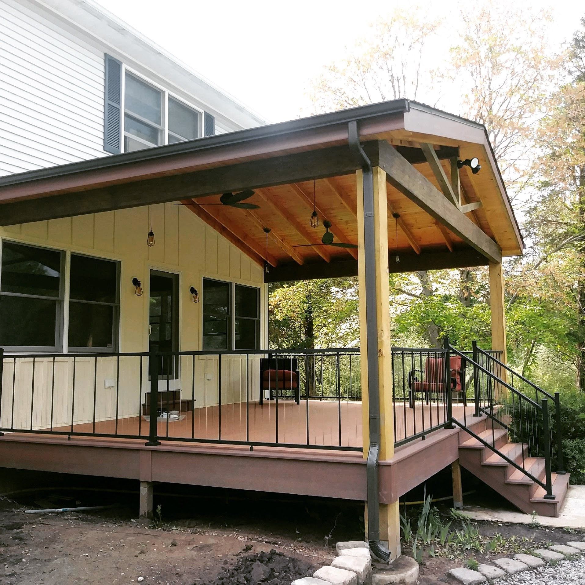Covered deck attached to a house with a brown deck, railing, and roof.