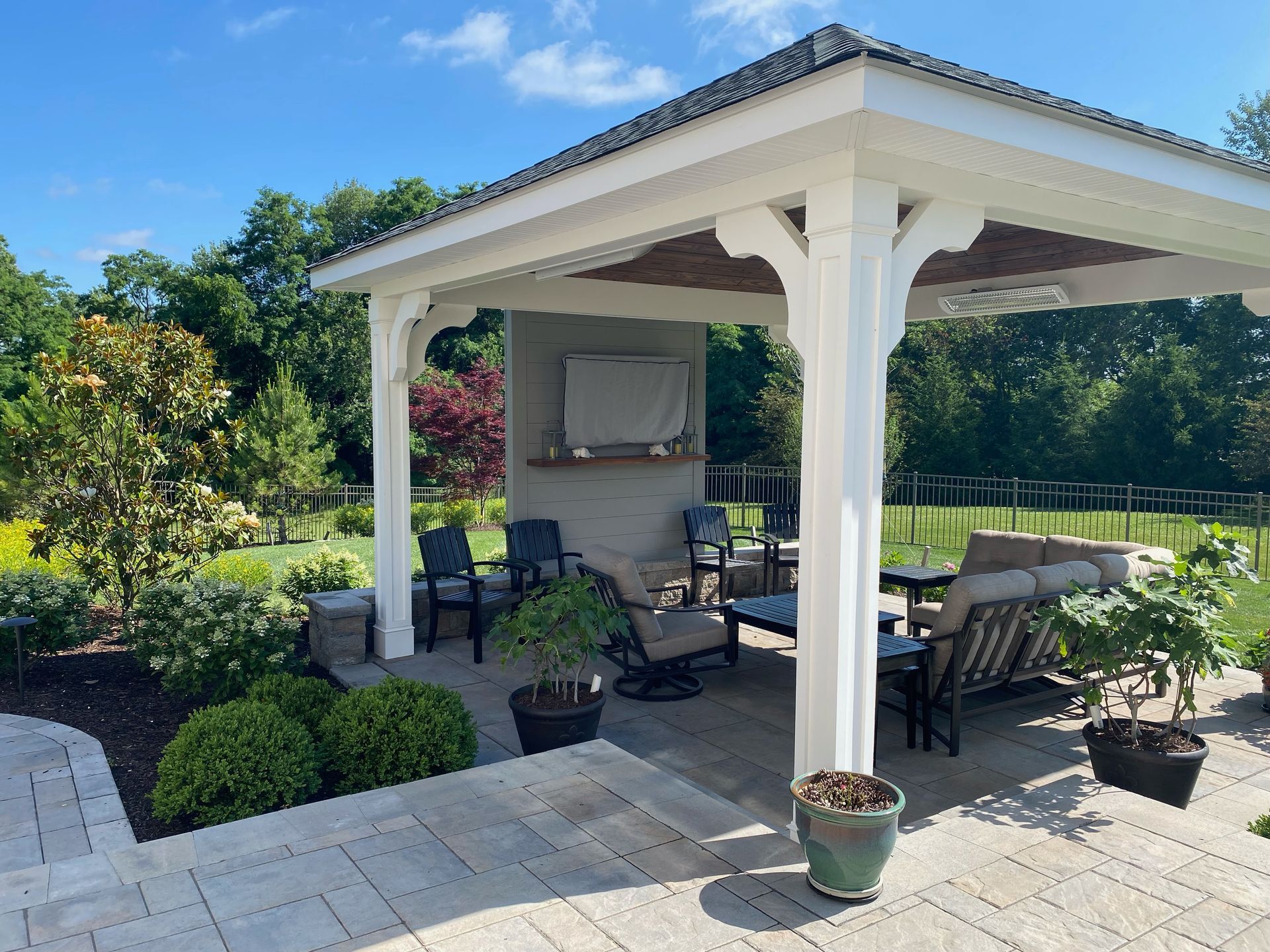 Outdoor patio with a white gazebo, seating, and landscaping under a sunny sky.