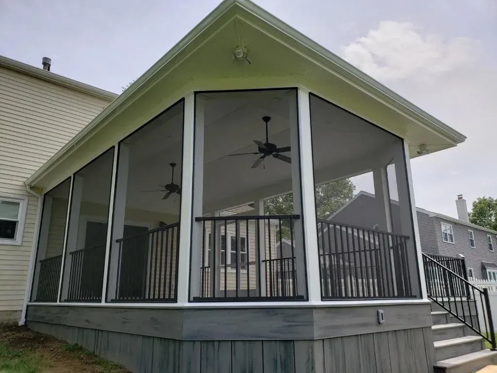 Screened-in porch addition with black screens, gray deck, white trim, and black railings; houses in background.