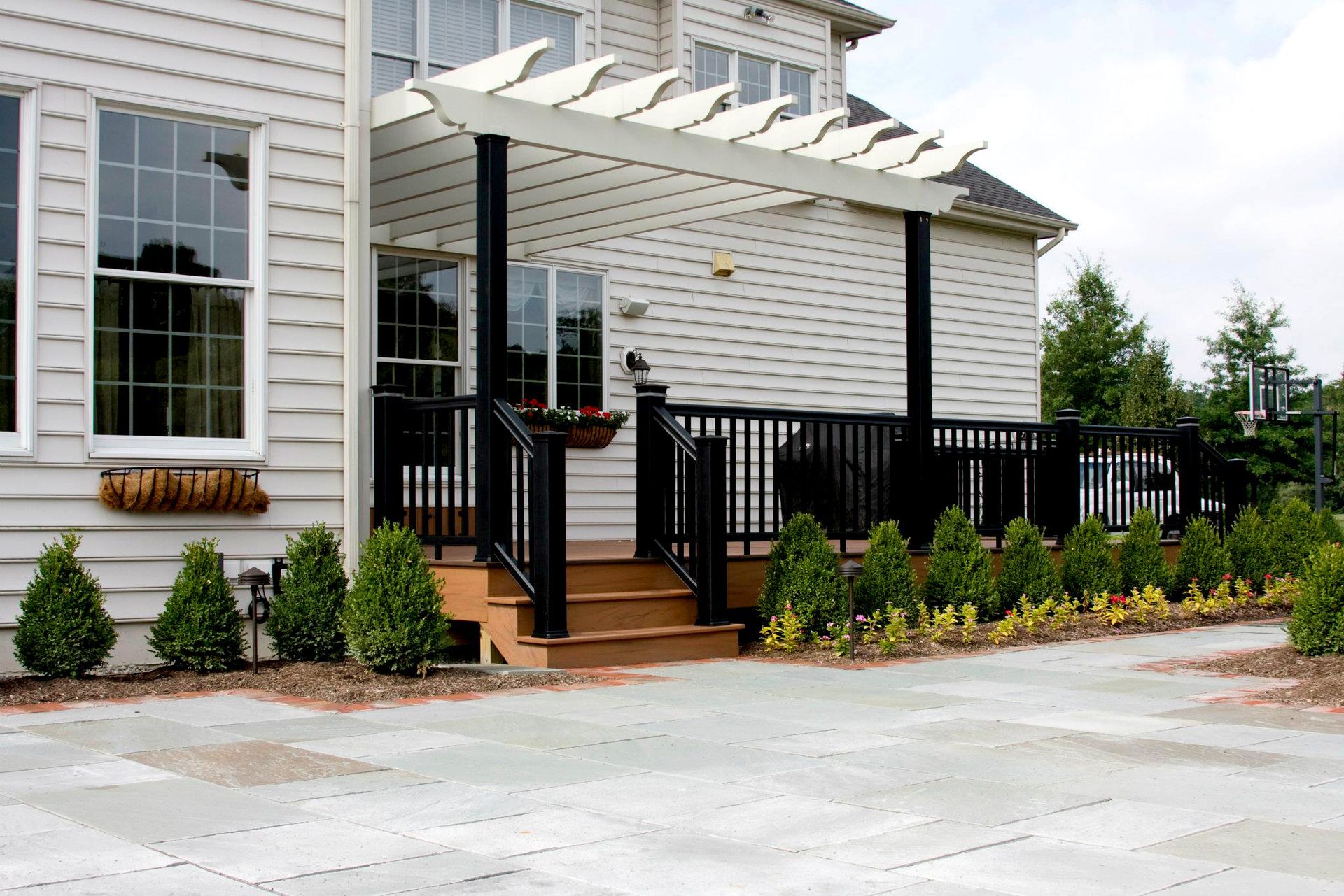 Back deck with pergola, black railings, and small bushes along the edge.