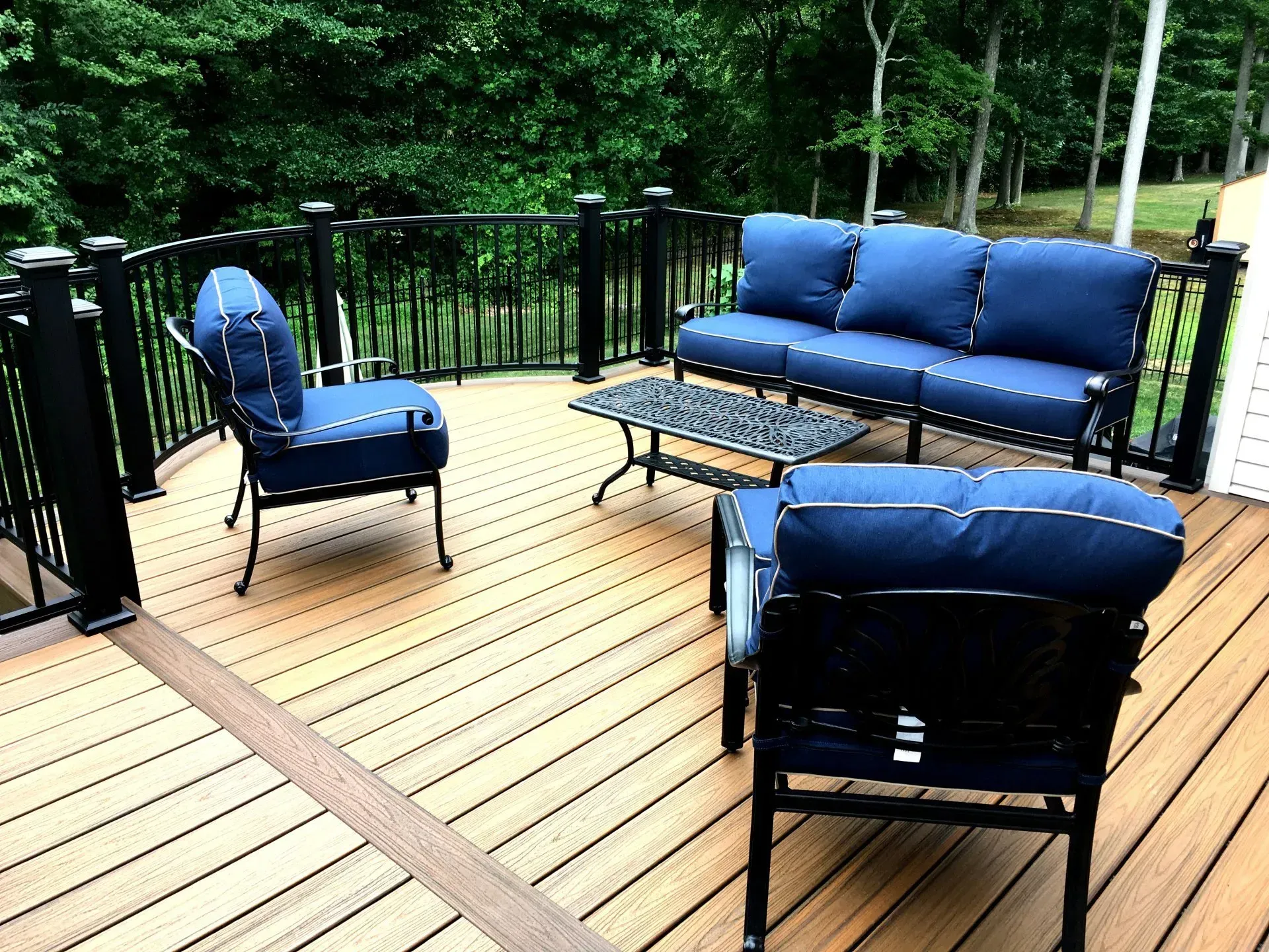Outdoor deck with black railing, brown composite decking, and blue cushioned furniture.