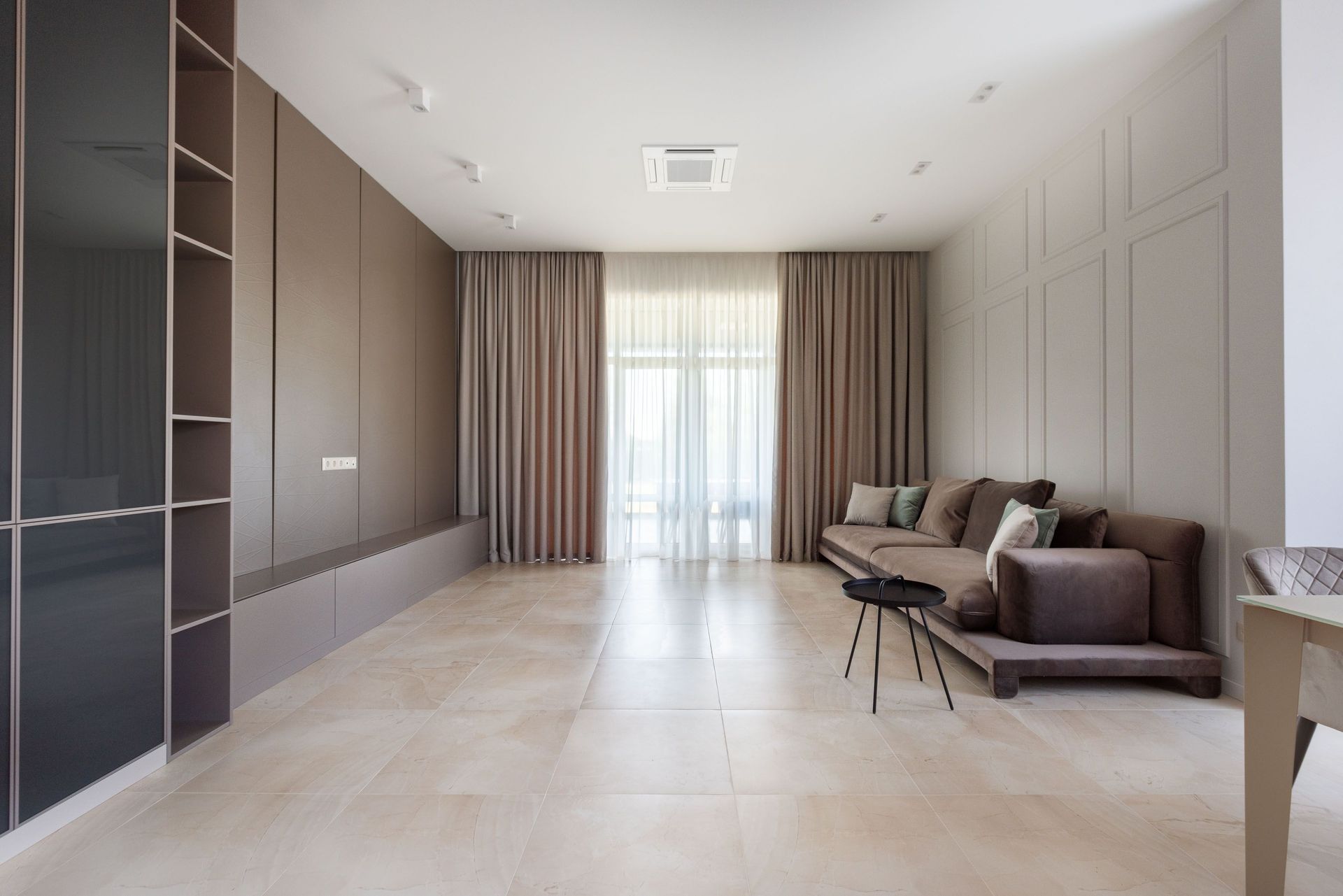 Modern minimalist living room with beige tile floors, gray sofa, curtains, and built-in wall cabinets