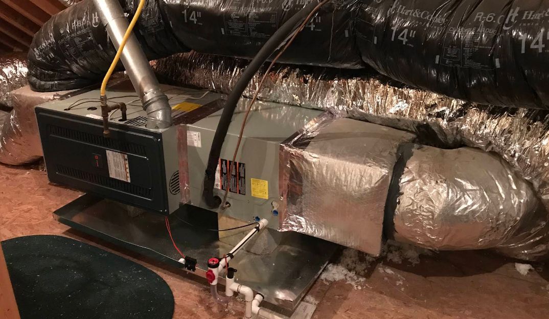 Basement HVAC furnace and ductwork with silver insulated vents and red gas valve on the floor