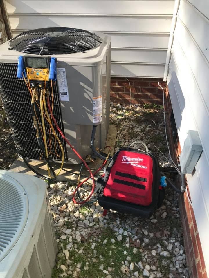 Outdoor HVAC unit with gauges and red service machine beside a house wall