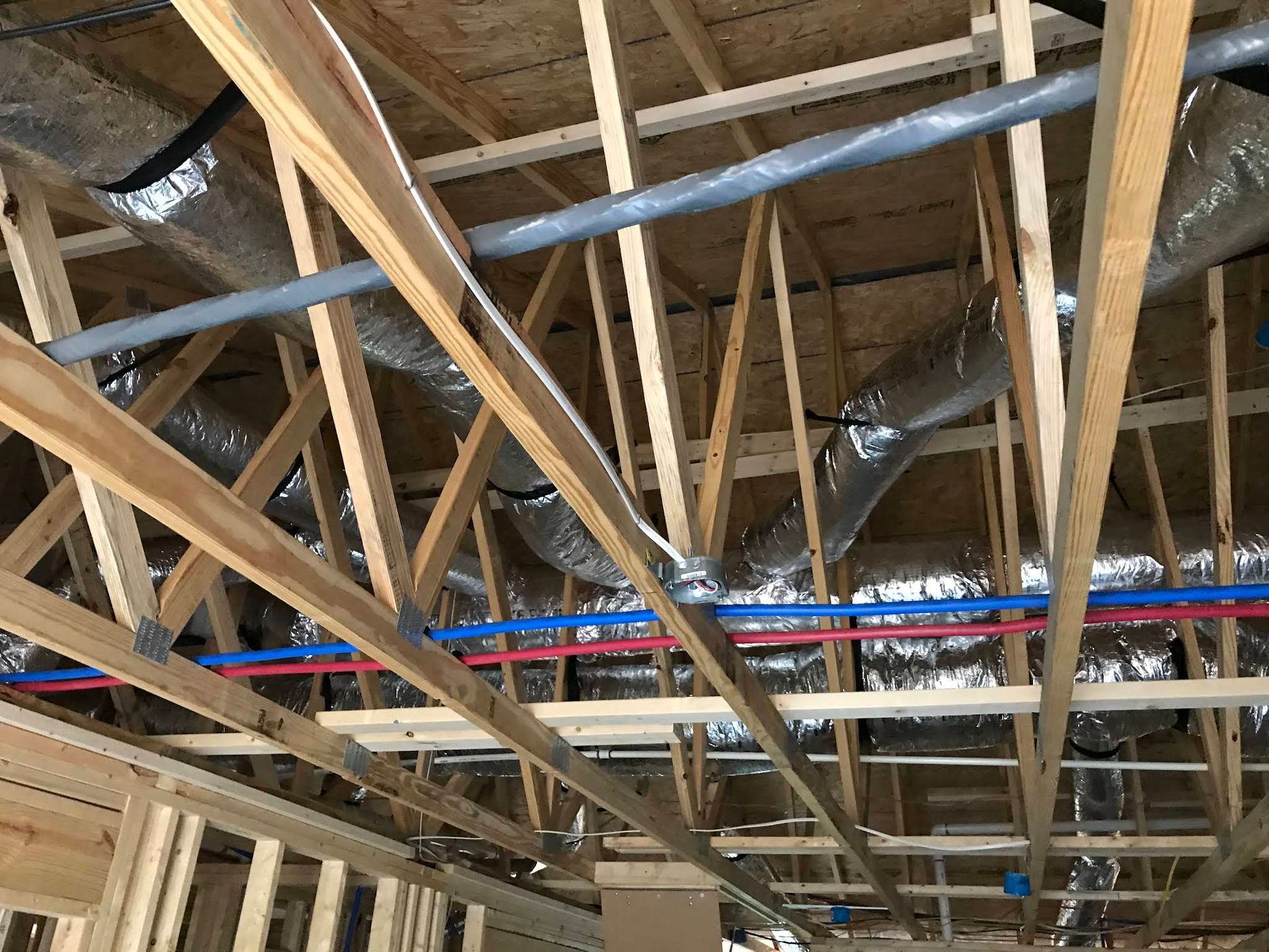 Exposed wooden roof framing with silver insulation and red-blue electrical piping overhead