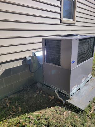 Outdoor HVAC unit beside a house with beige siding, sitting on a concrete pad near a small utility box