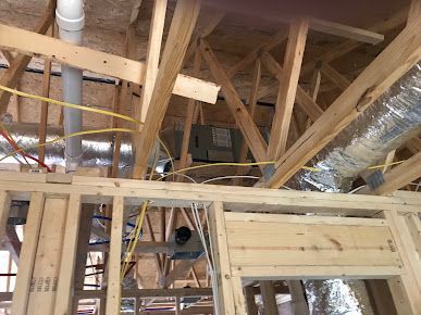 Exposed attic framing with wooden trusses, ductwork, and insulation in an unfinished house interior