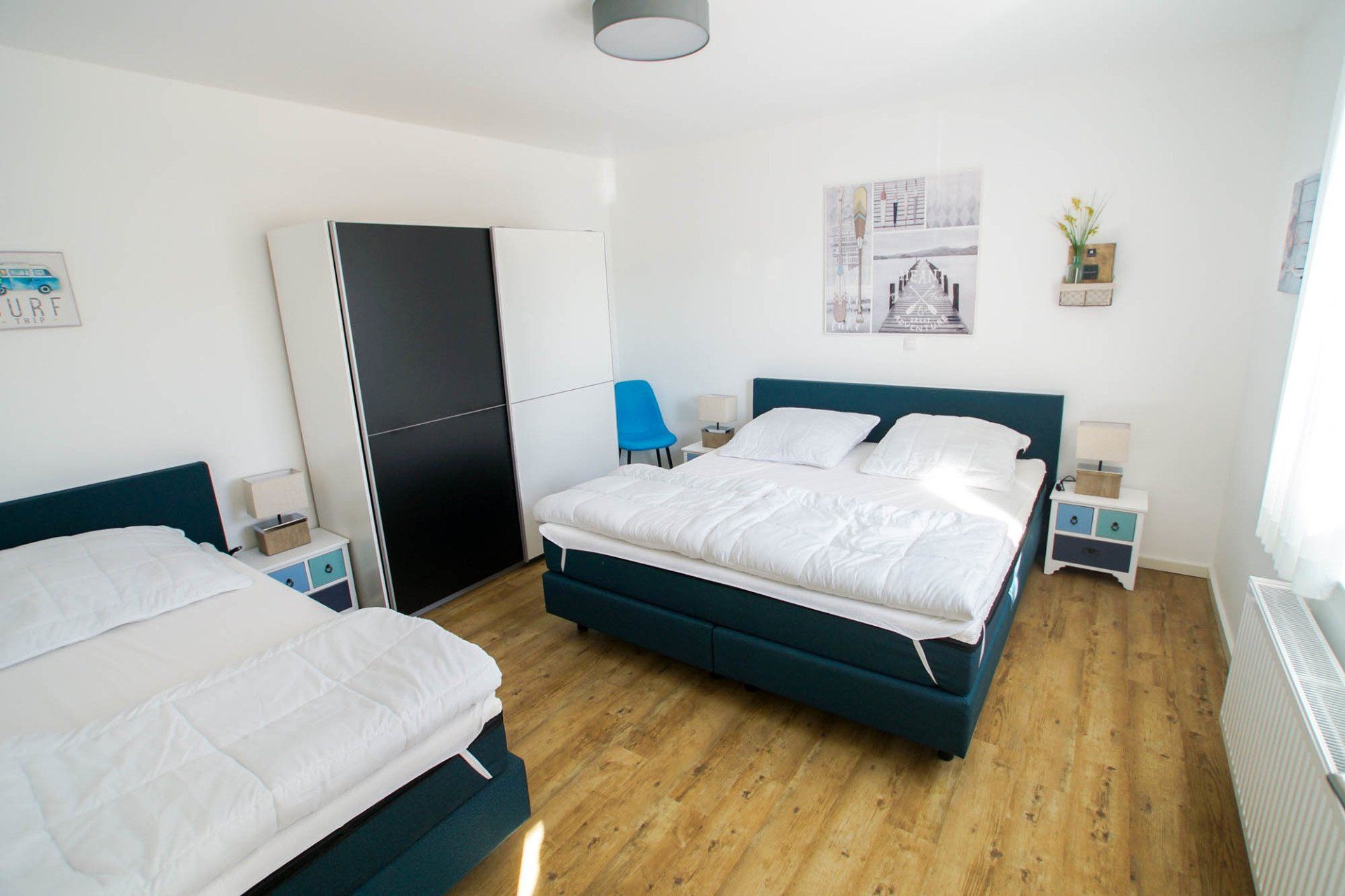 Schlafzimmer mit zwei Betten, großem Kleiderschrank, Nachttischen und Dekorationsobjekten. Holzboden und helle Wände.