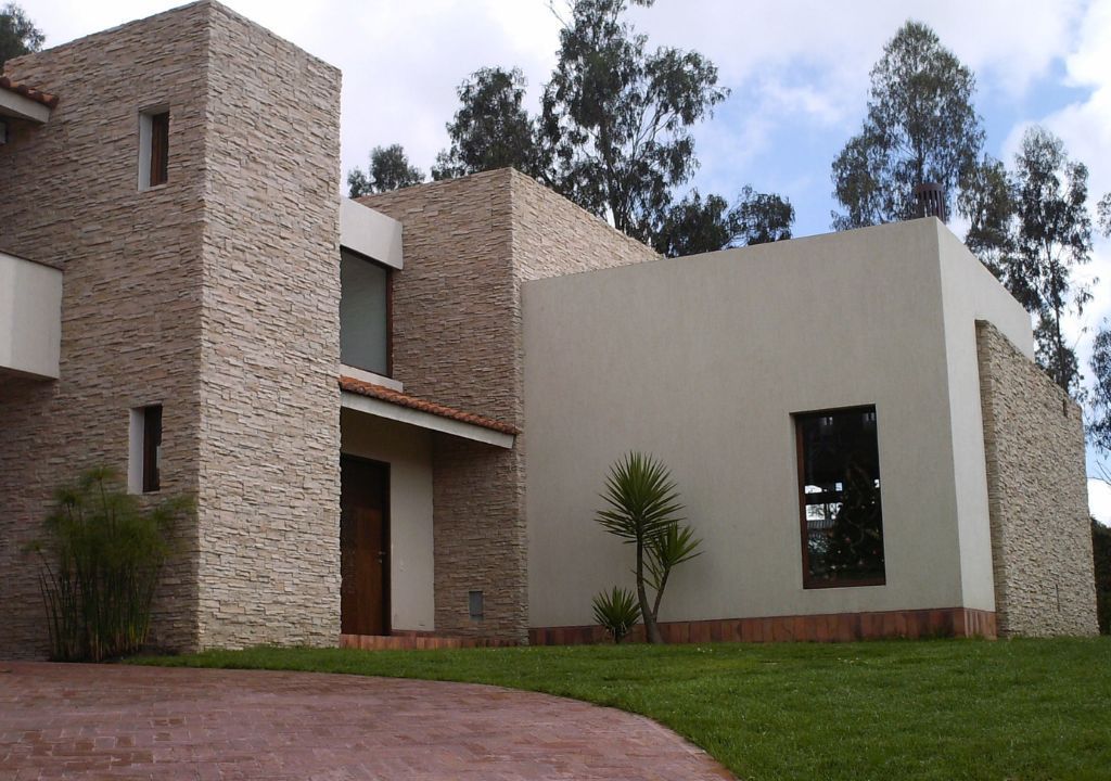 Exterior de una casa moderna con paredes de piedra y blancas, techo de tejas rojas y entrada curva.
