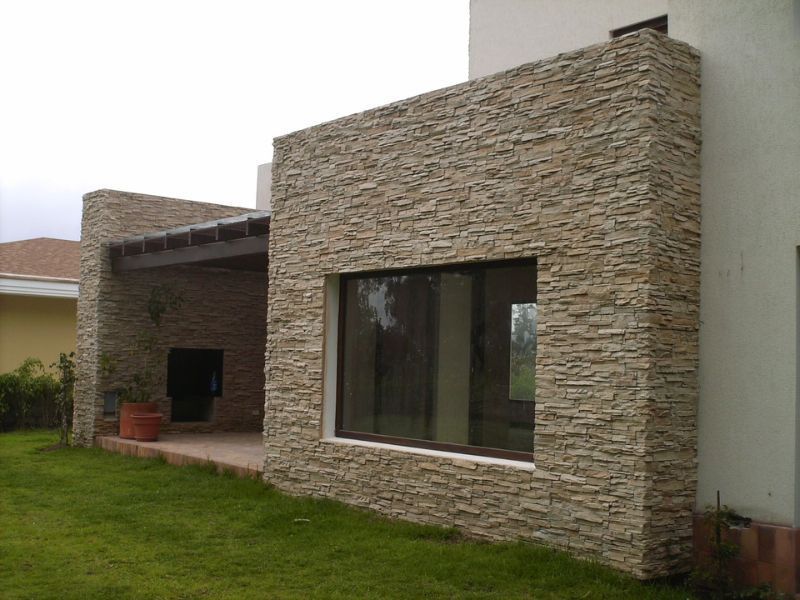 Exterior de una casa moderna revestida de piedra con una gran ventana y césped.