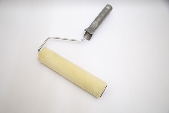 Rodillo de pintura con cubierta de espuma blanca y mango gris sobre fondo claro.