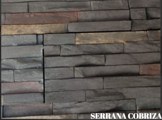 Pared decorativa de piedra detrás de un sillón reclinable negro en una habitación con poca luz, con una planta