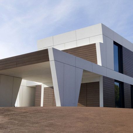 Edificio geométrico moderno con paneles blancos y marrones, soportes angulares y un fondo de cielo azul.