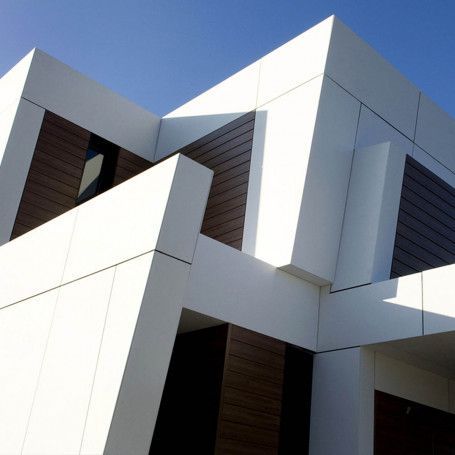 Edificio geométrico moderno con paneles blancos y marrones, soportes angulares y un fondo de cielo azul.