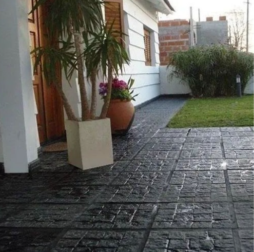 Patio pavimentado junto a una casa blanca con plantas en macetas y un jardín con césped.