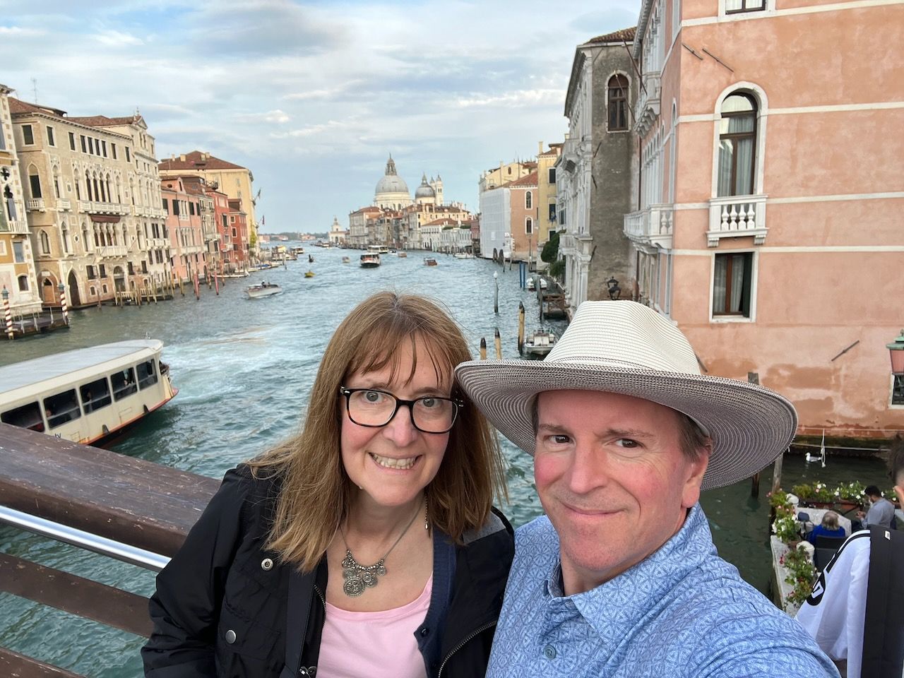 Two people smiling on a bridge in Venice with a canal and boats behind them