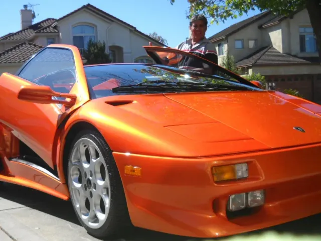 Orange Lamborghini Diablo with a person wiping the windshield in front of a house.
