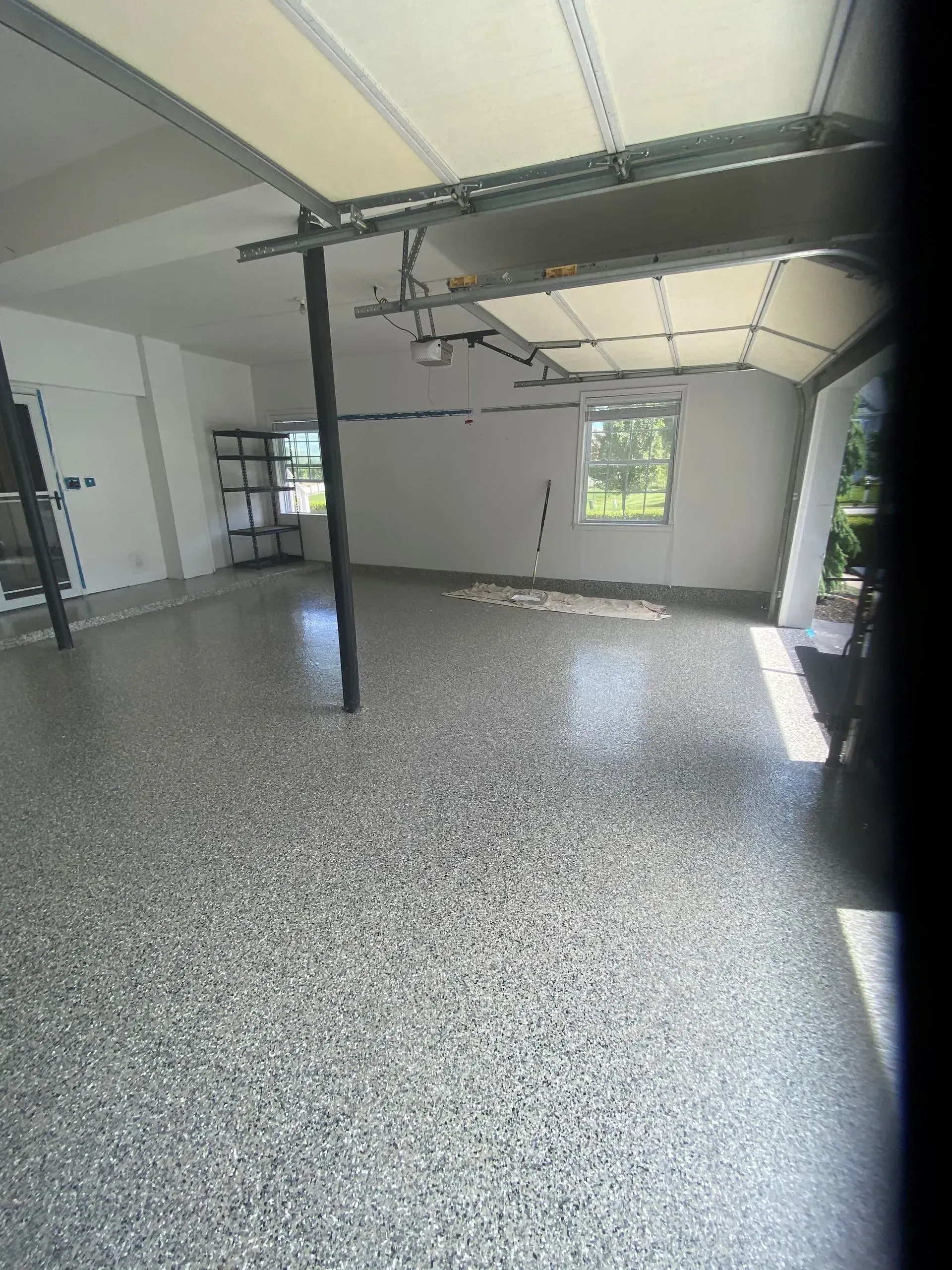 Empty garage with epoxy-coated floor, white walls, open garage door, and a single support beam.