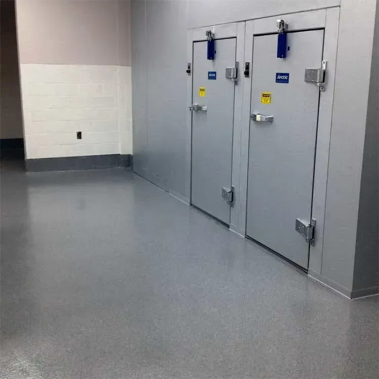 A hallway with two large, silver storage doors on the right and a gray floor.