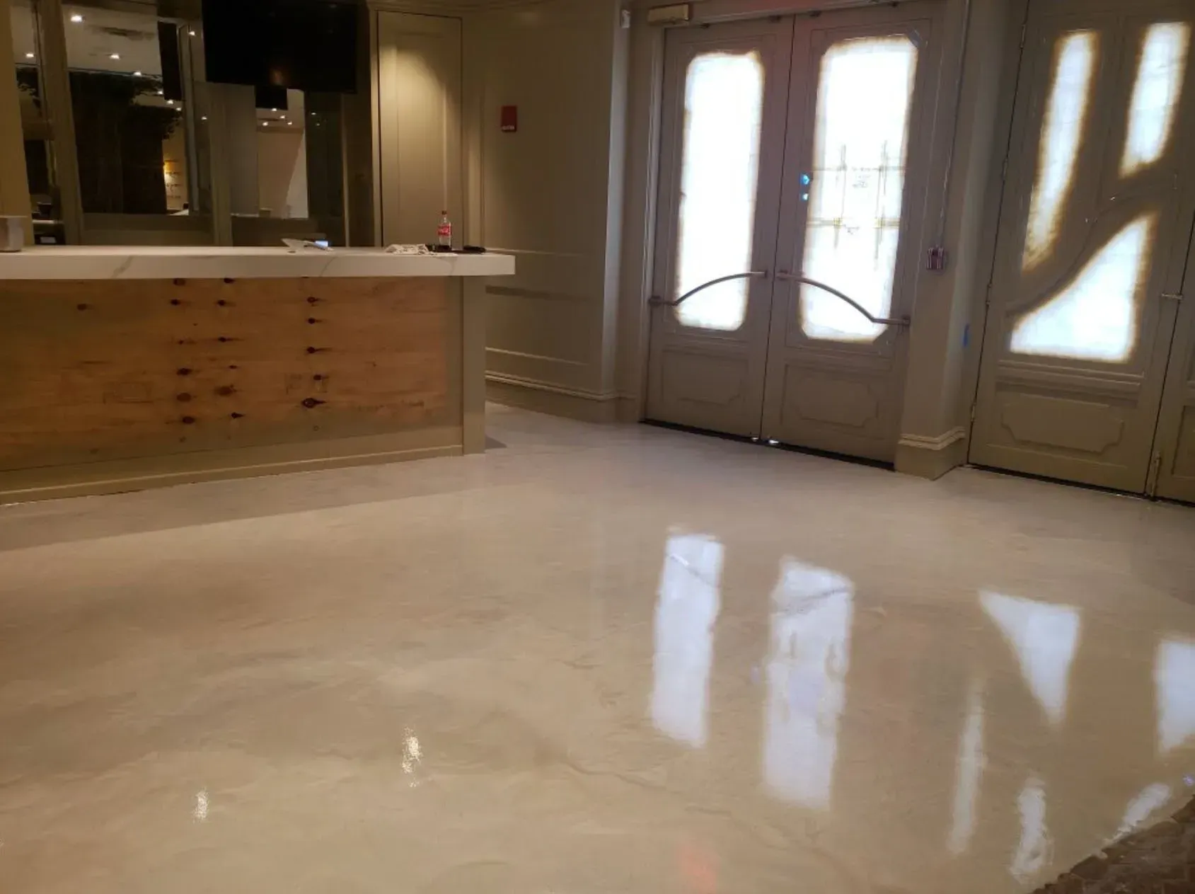 Shiny, light-colored floor in a room with a counter on the left and double doors with light coming through on the right.