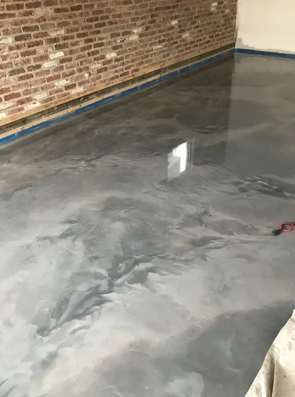 Metallic gray epoxy flooring reflects light, next to a brick wall.