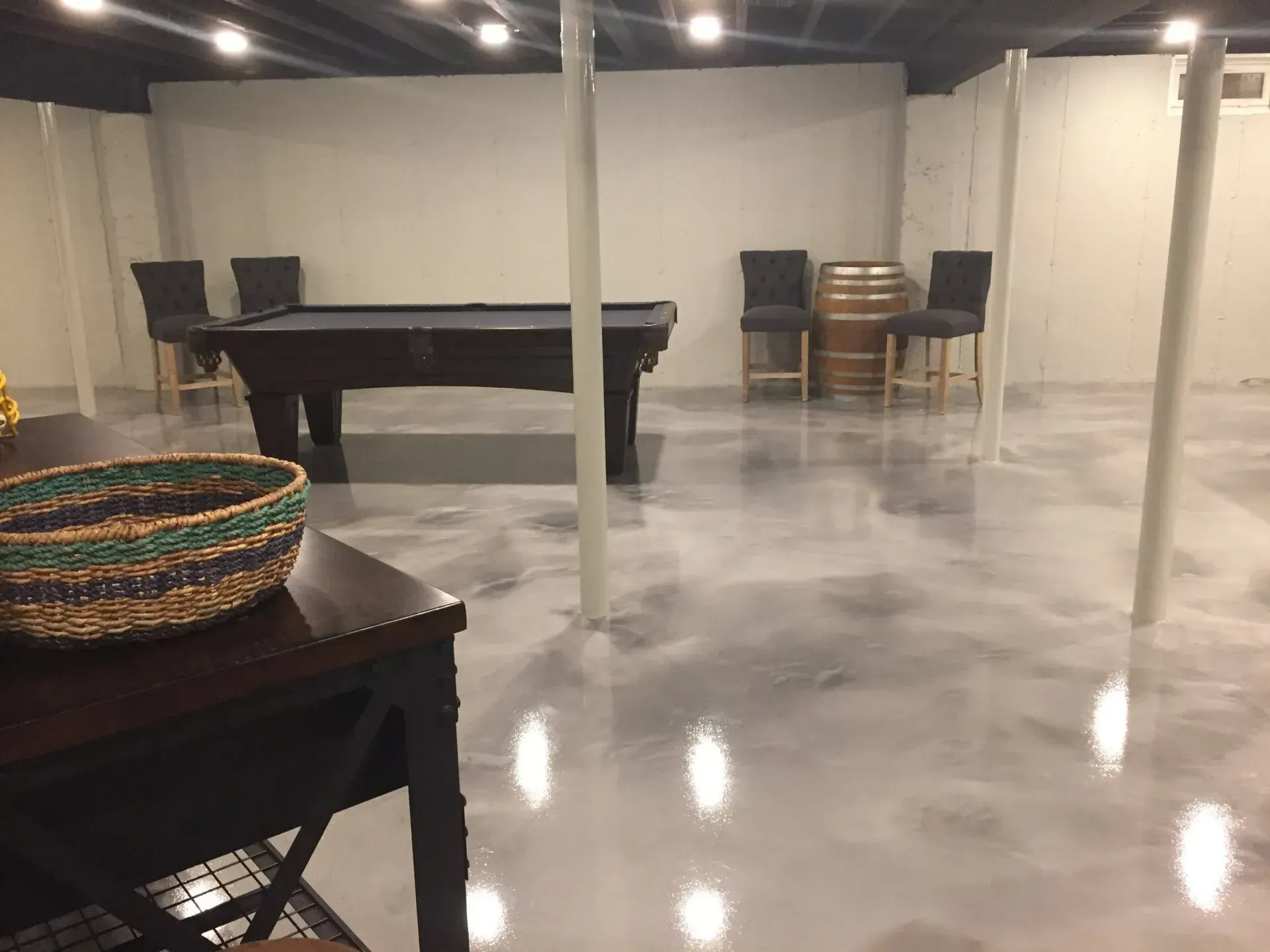 A finished basement with a pool table, stools, and a metallic-looking floor.