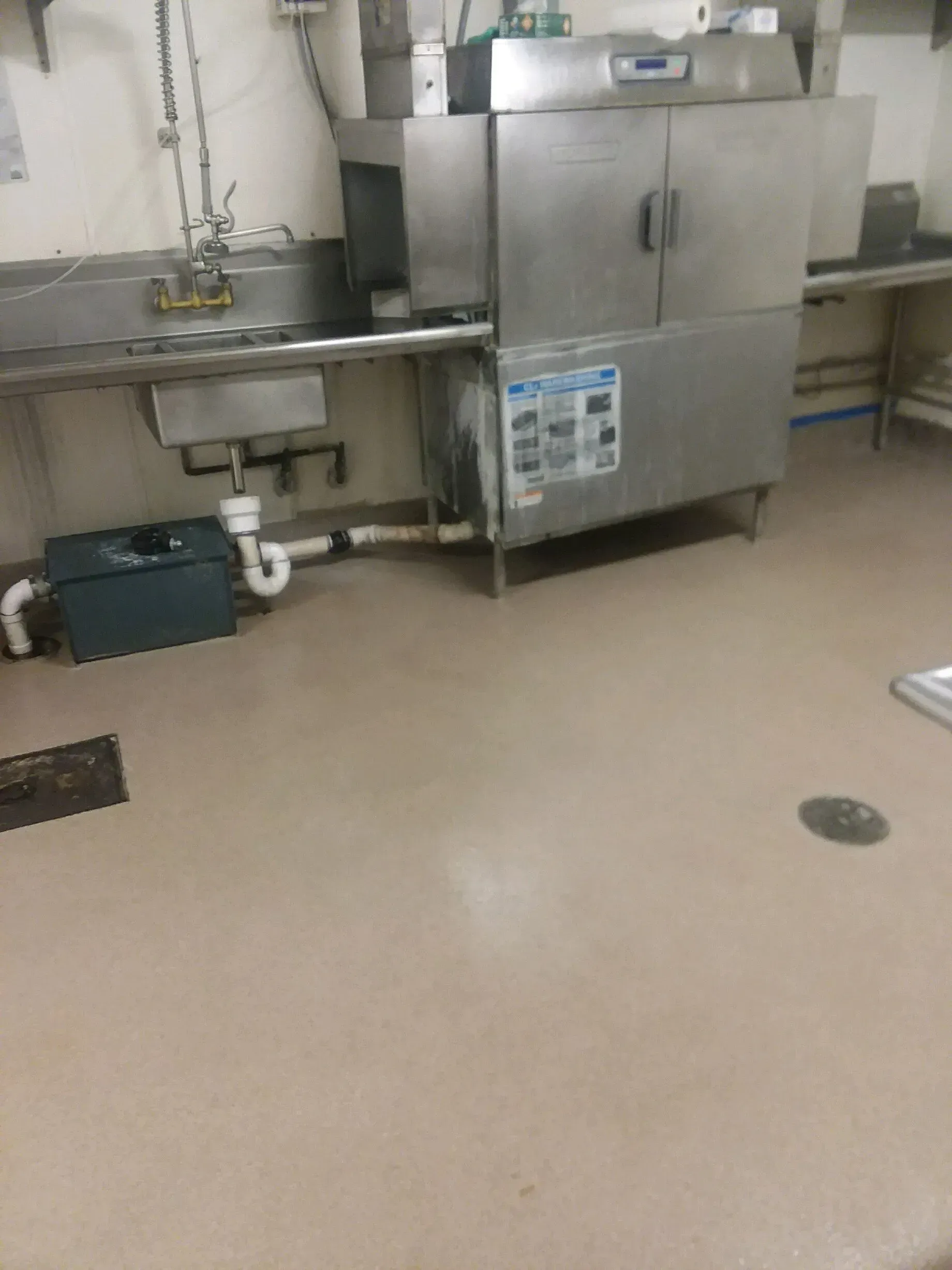Stainless steel commercial dishwasher in a kitchen with a sink and a black box.