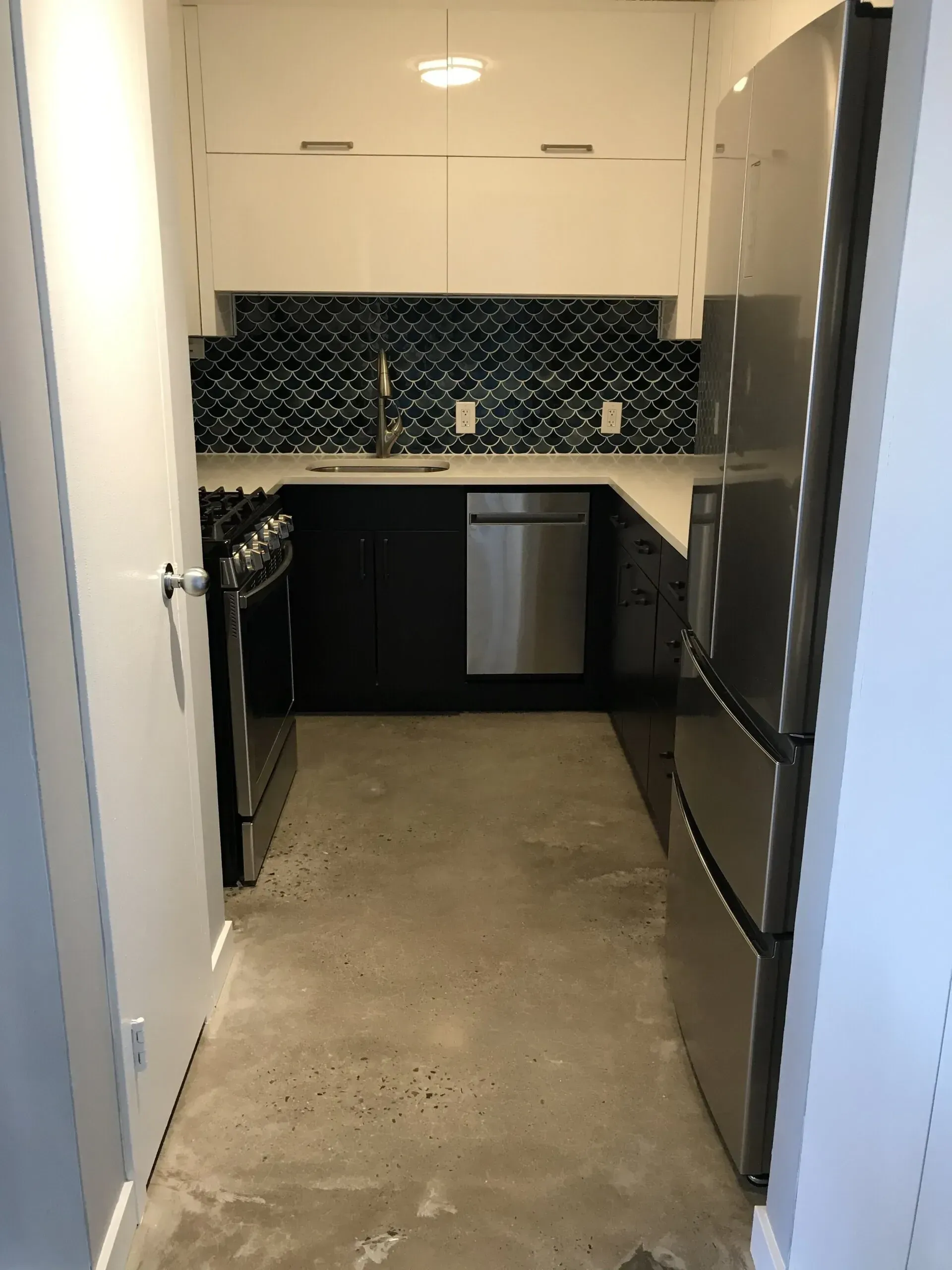 Small kitchen with dark cabinets, stainless steel appliances, and blue tiled backsplash.