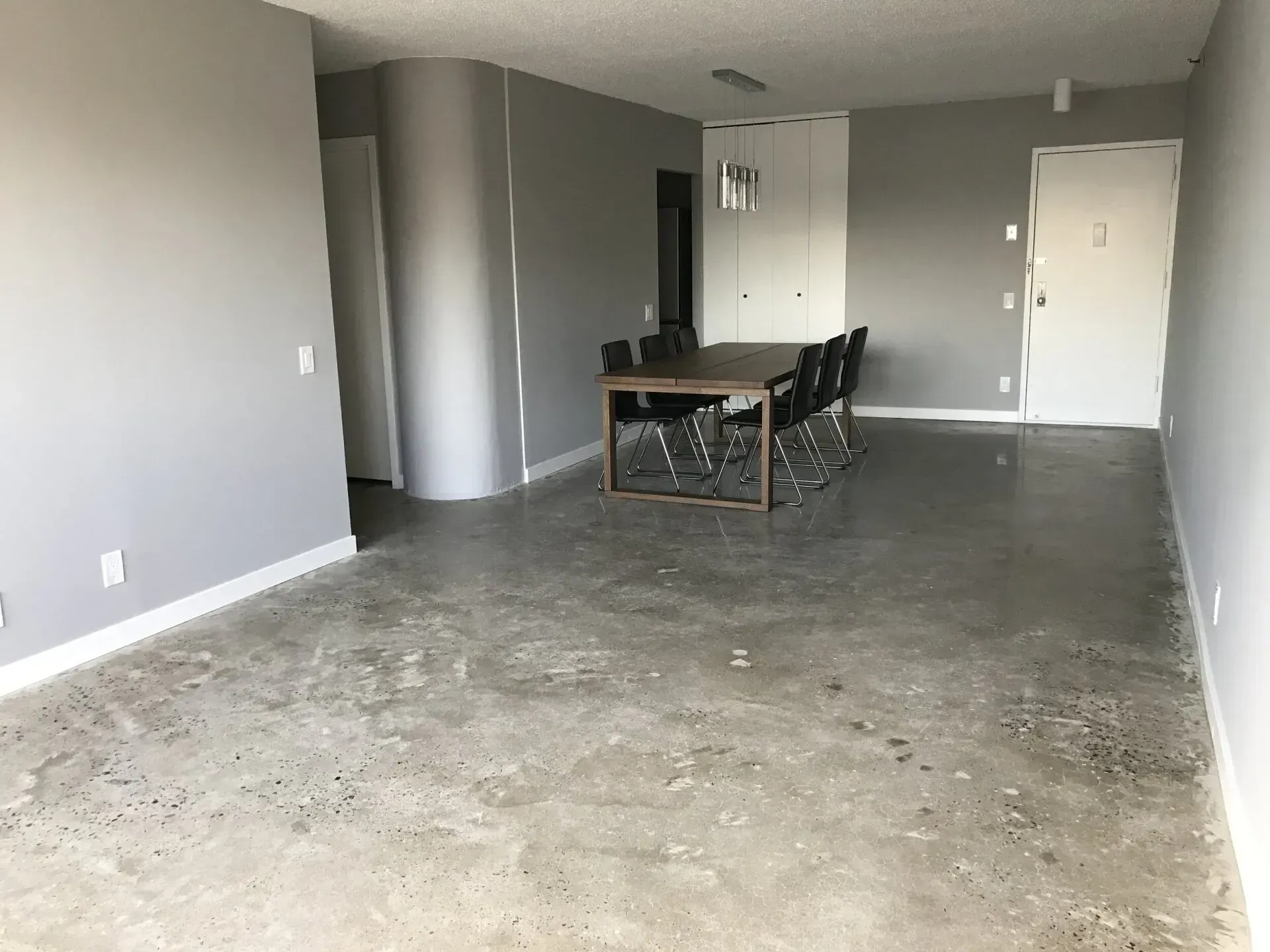 Empty room with concrete floor, gray walls, dining table, and doors.