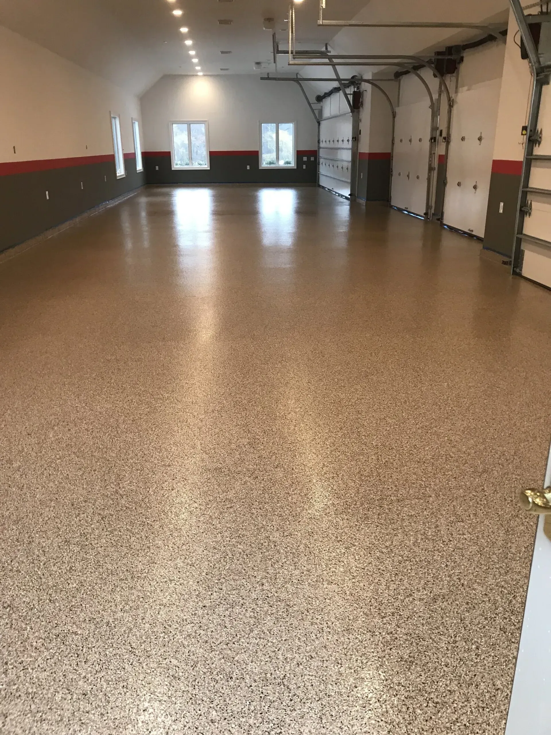 Spacious garage with speckled epoxy floor, white walls, gray and red trim, and three garage doors.