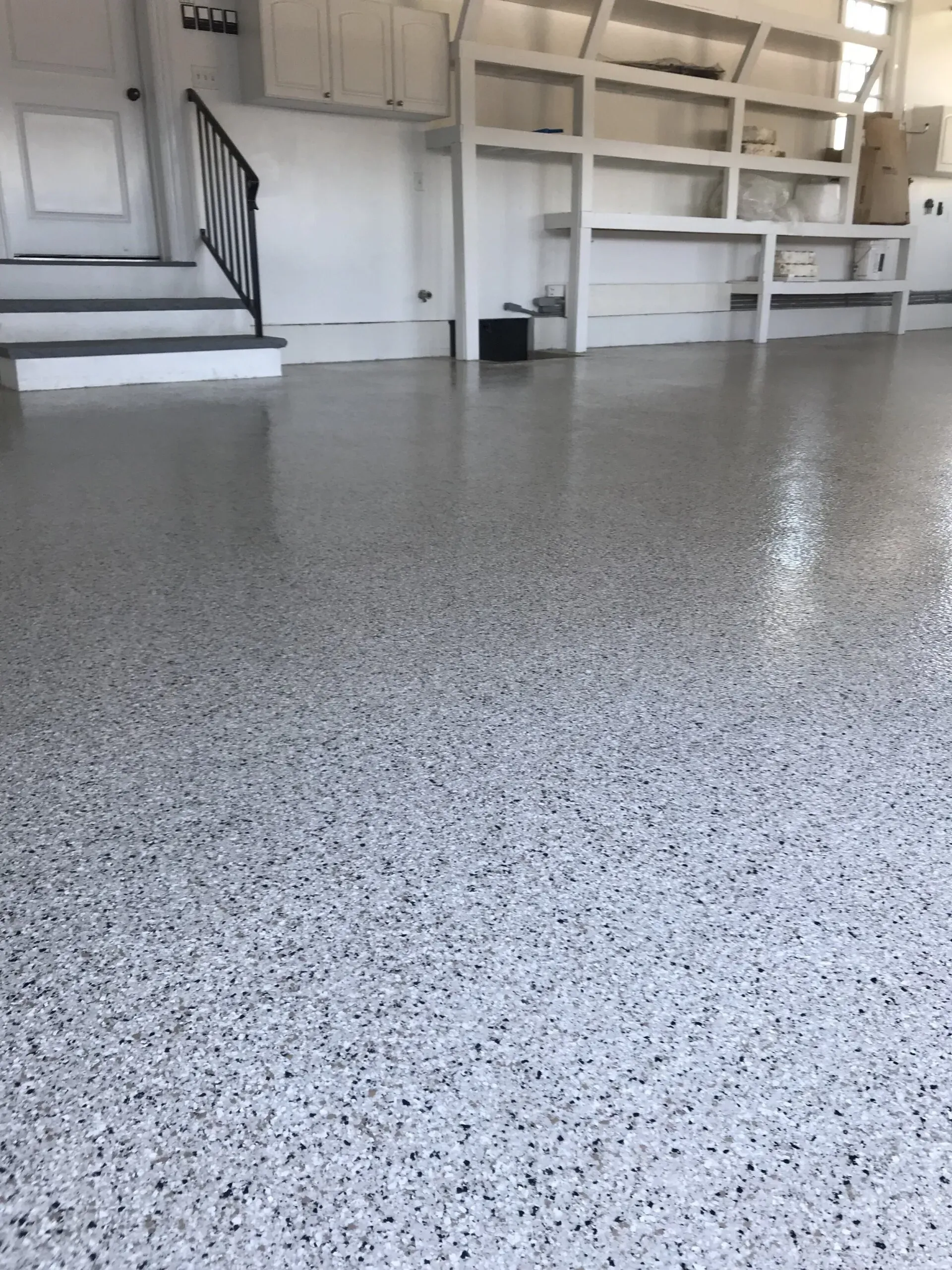 Garage floor with a speckled epoxy coating, reflecting the room's white walls and built-in storage.