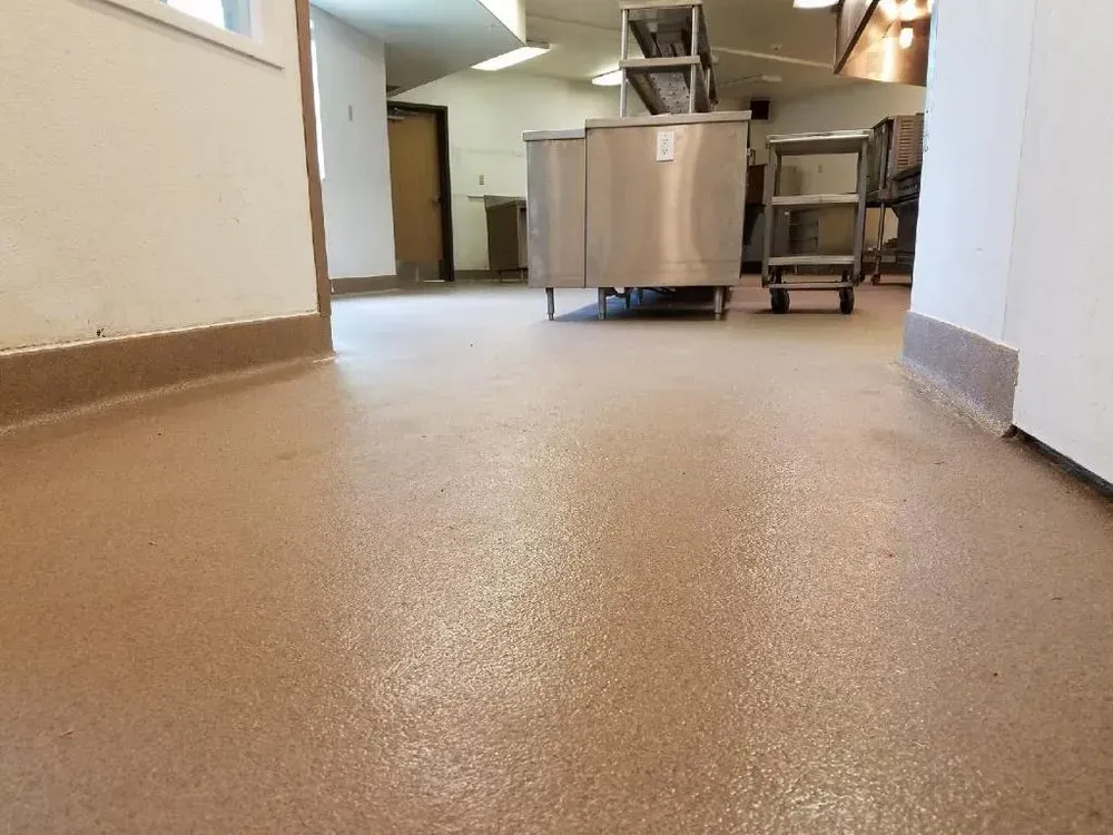 A commercial kitchen with beige flooring, stainless steel equipment, and white walls.