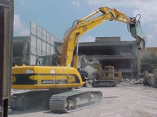 Yellow excavator demolishing a building, lifting debris at a construction site