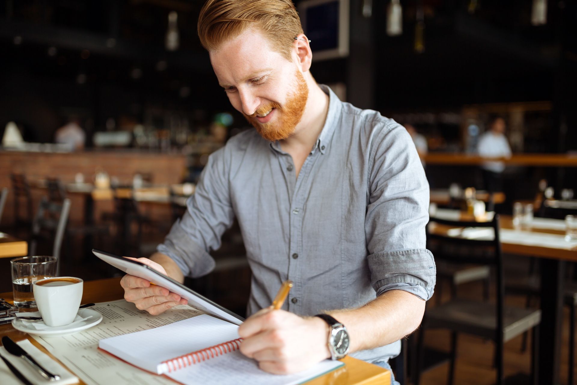 A man is sitting at a table in a restaurant writing in a notebook.