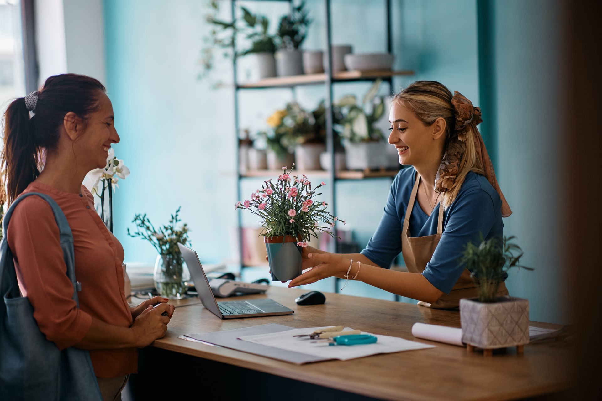 Two women are sitting at a table talking to each other in a flower shop.