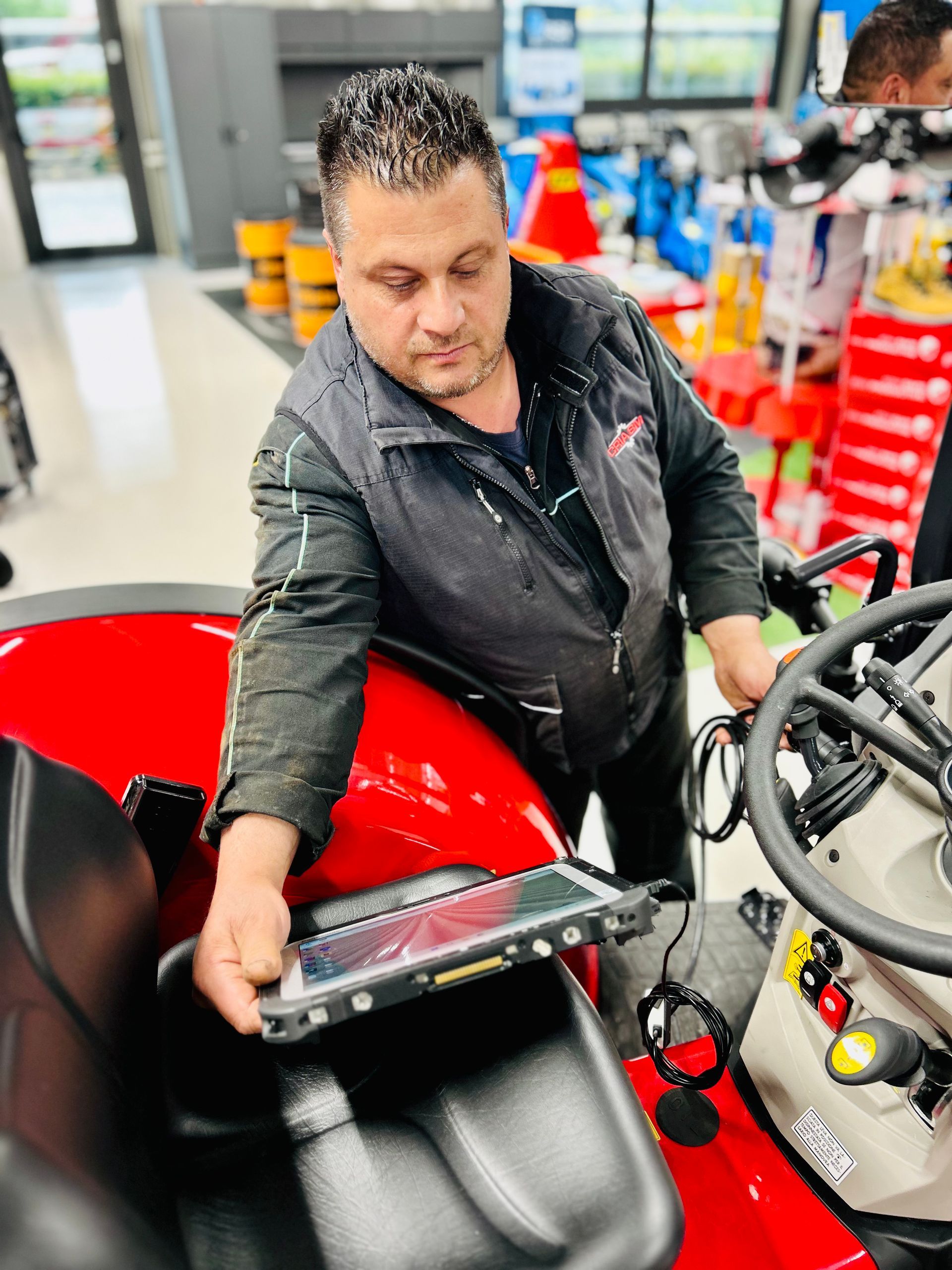 Uomo che usa un tablet per diagnosticare un trattore rosso in un negozio.