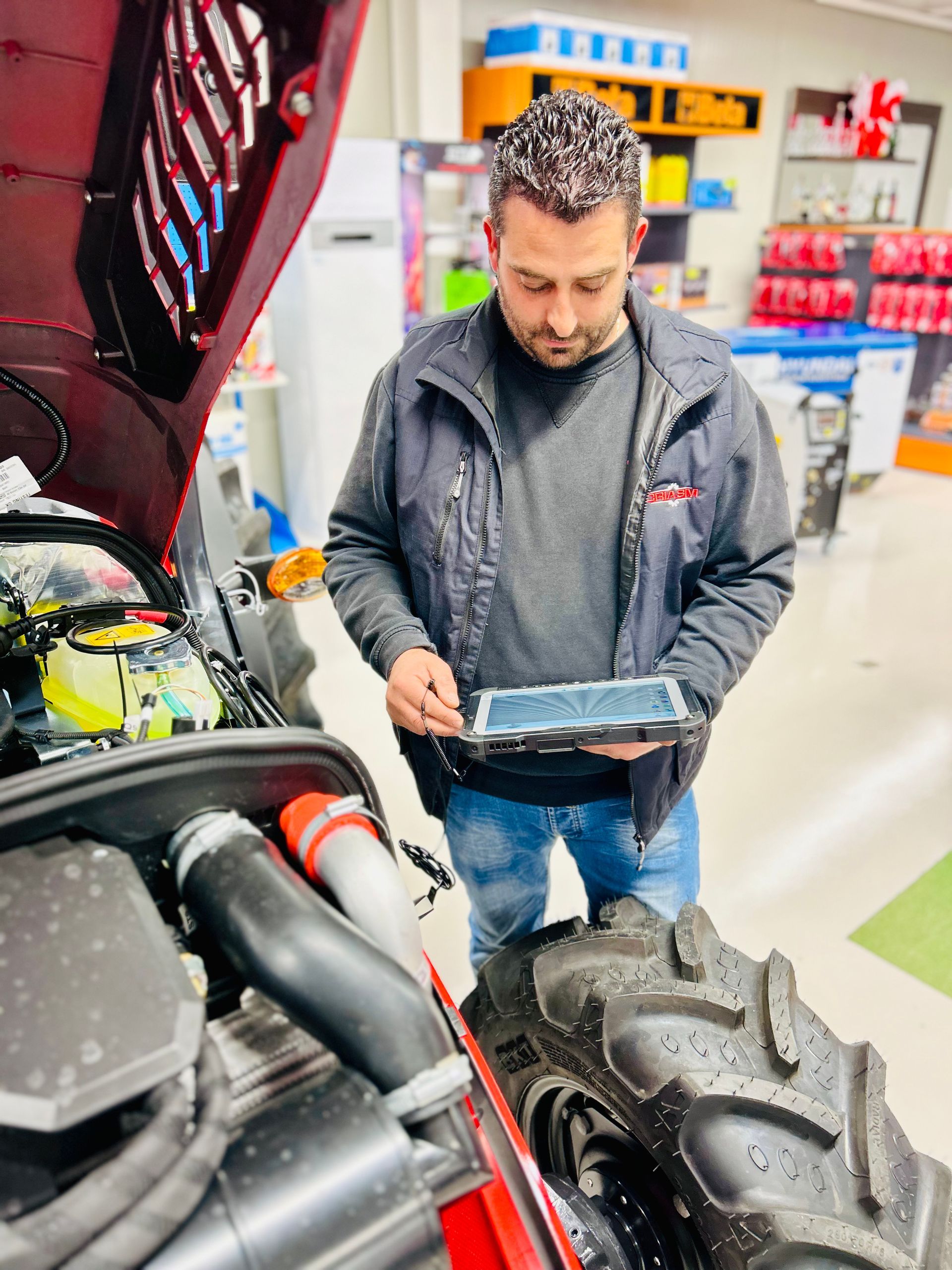Uomo che utilizza un tablet per ispezionare il motore di un trattore in un negozio.